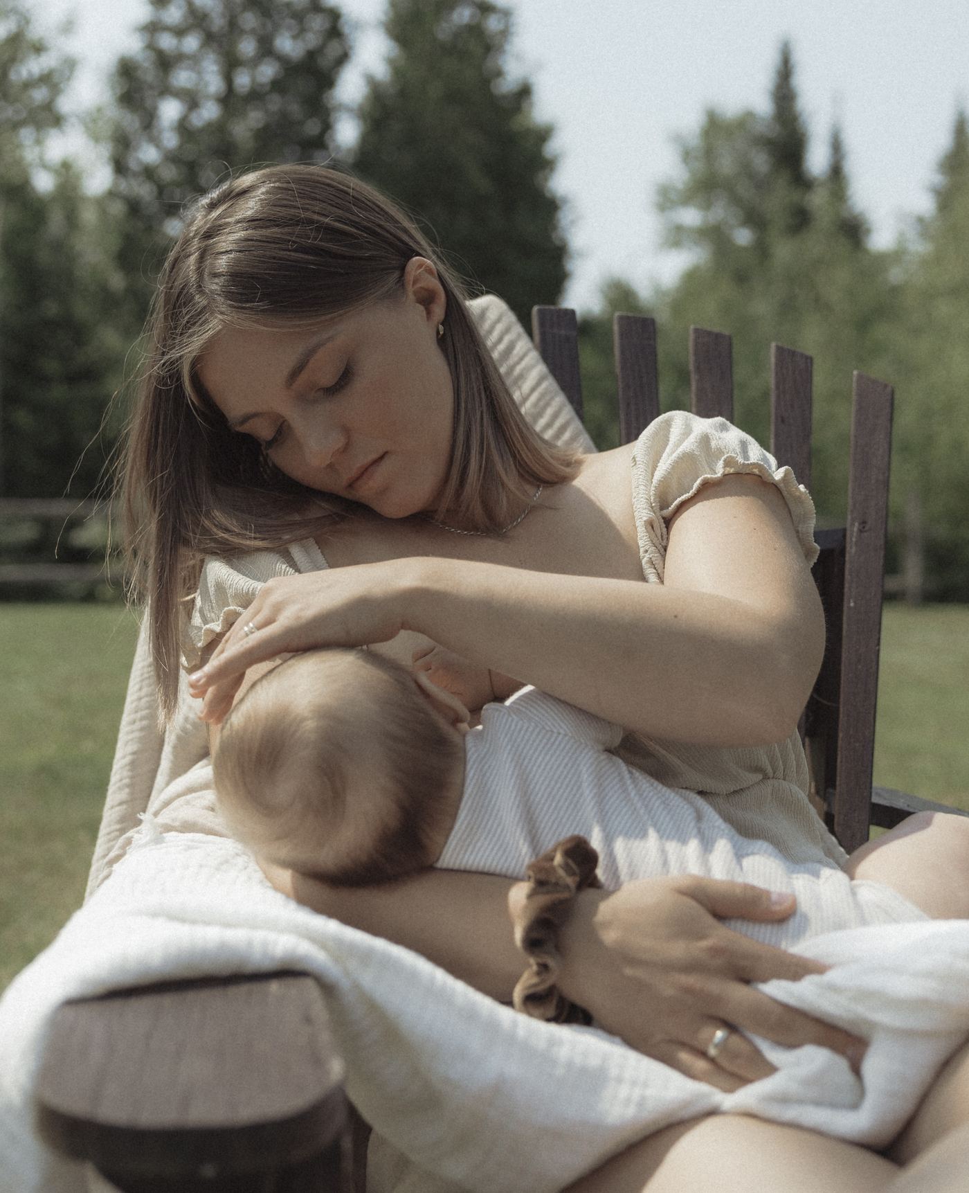 Mère qui allaite son bébé, assise dehors sur une chaise de bois