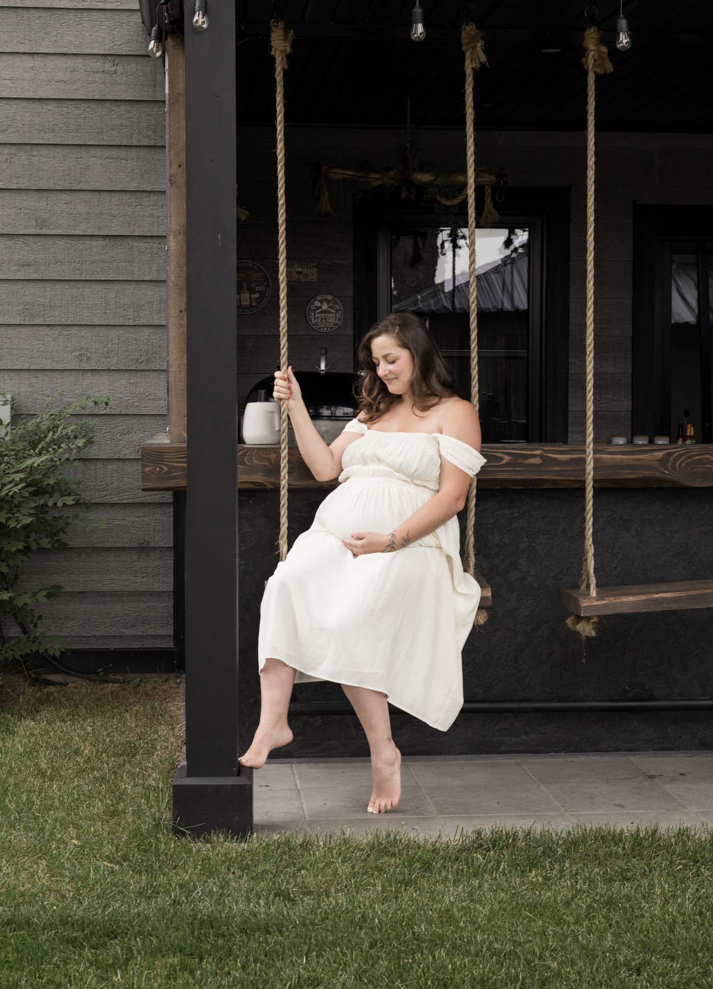 Femme enceinte en robe blanche assise sur une balançoire de galerie