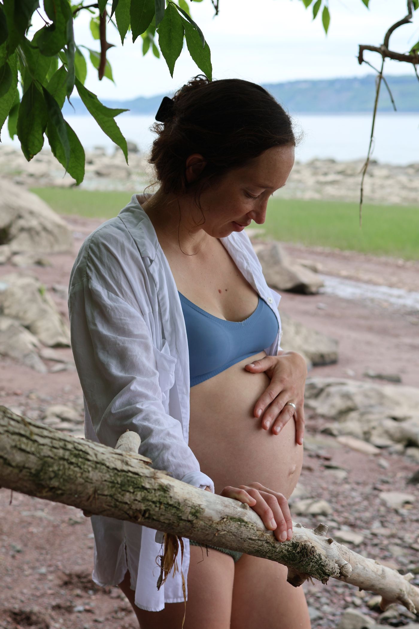 Femme enceinte appuyée sur un tronc de bois flotté, le fleuve derrière