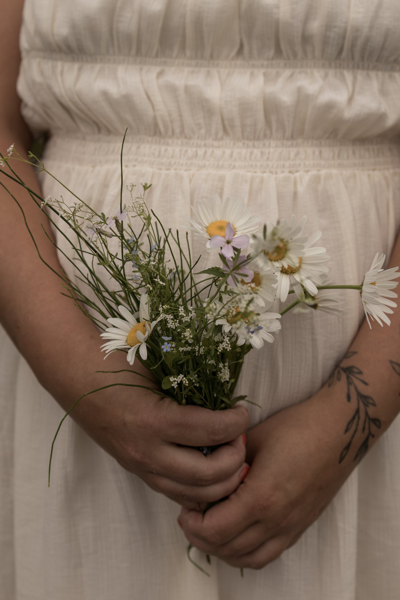 Bouquet de marguerites sauvages tenu devant une robe crème