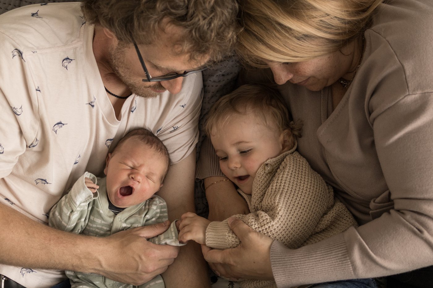 Deux parents penchés autour de leur nouveau-né qui bâille et de leur aîné