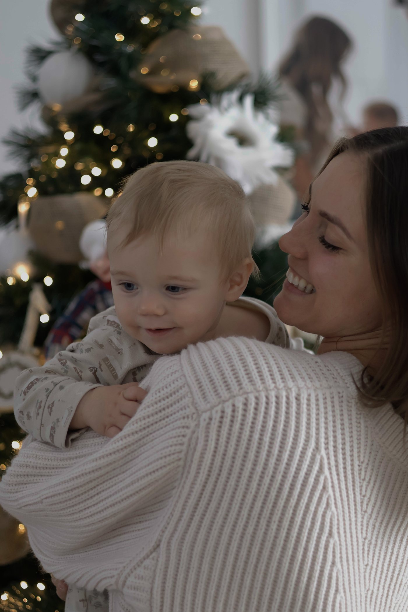 Mere qui embrasse son bebe devant des lumieres de Noel