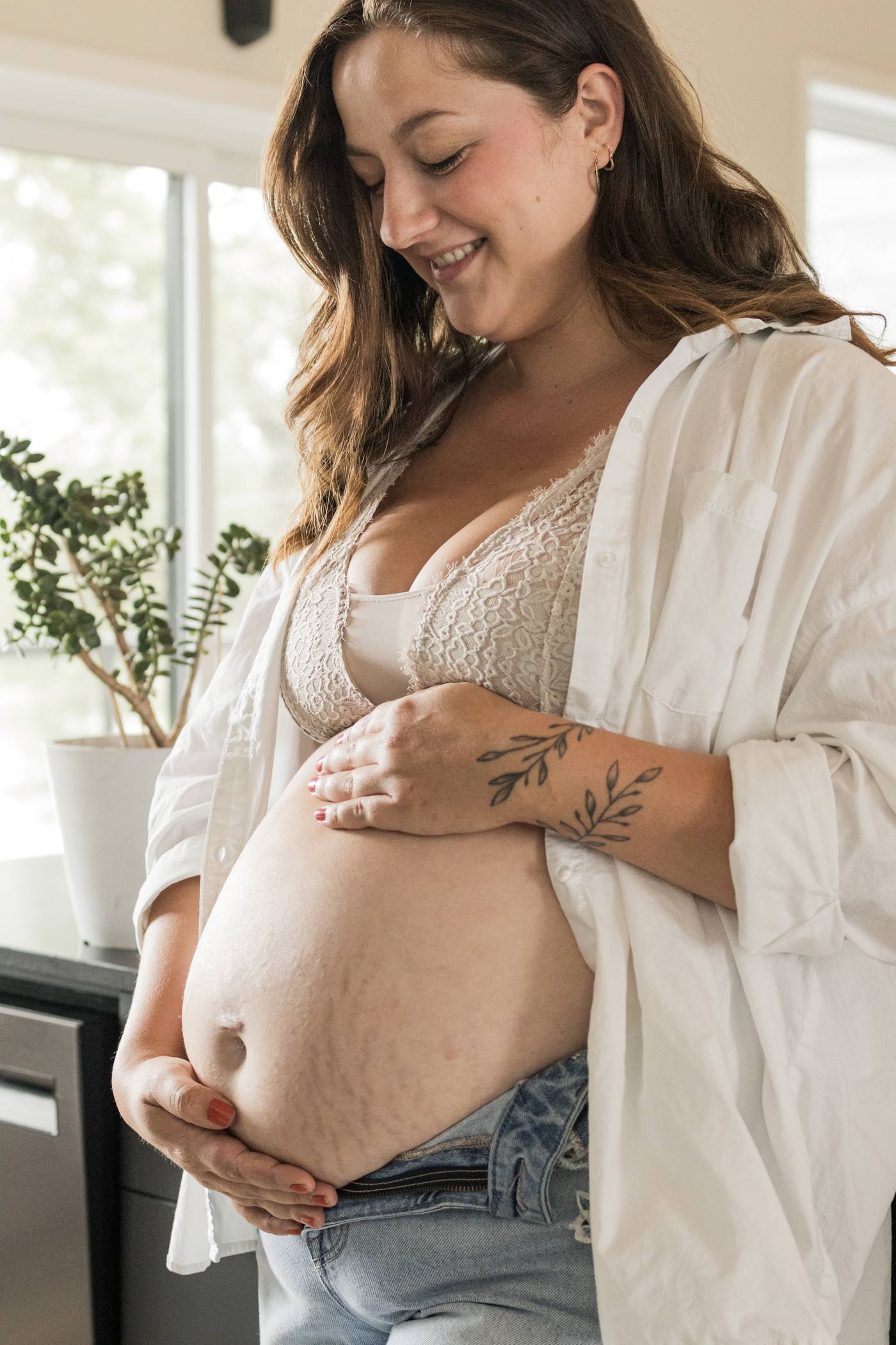 Femme enceinte qui sourit en tenant son ventre, chez elle près de ses plantes