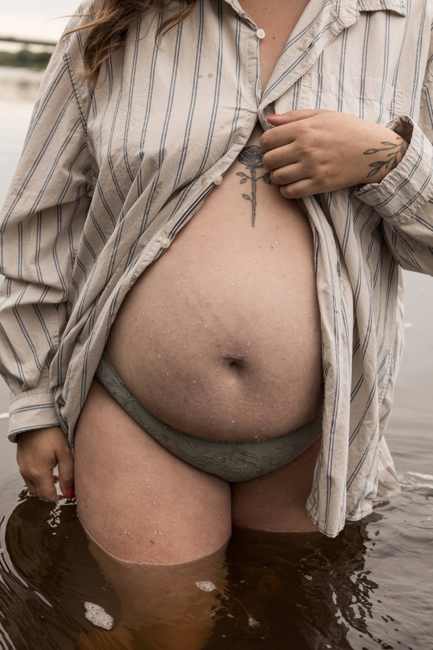 Ventre rond sous une chemise rayée ouverte, debout dans l'eau